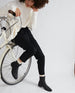 Woman leaned on the front of a bicycle wearing a white long sleeve shirt with black pants and the Miki Boot in Black.  6
