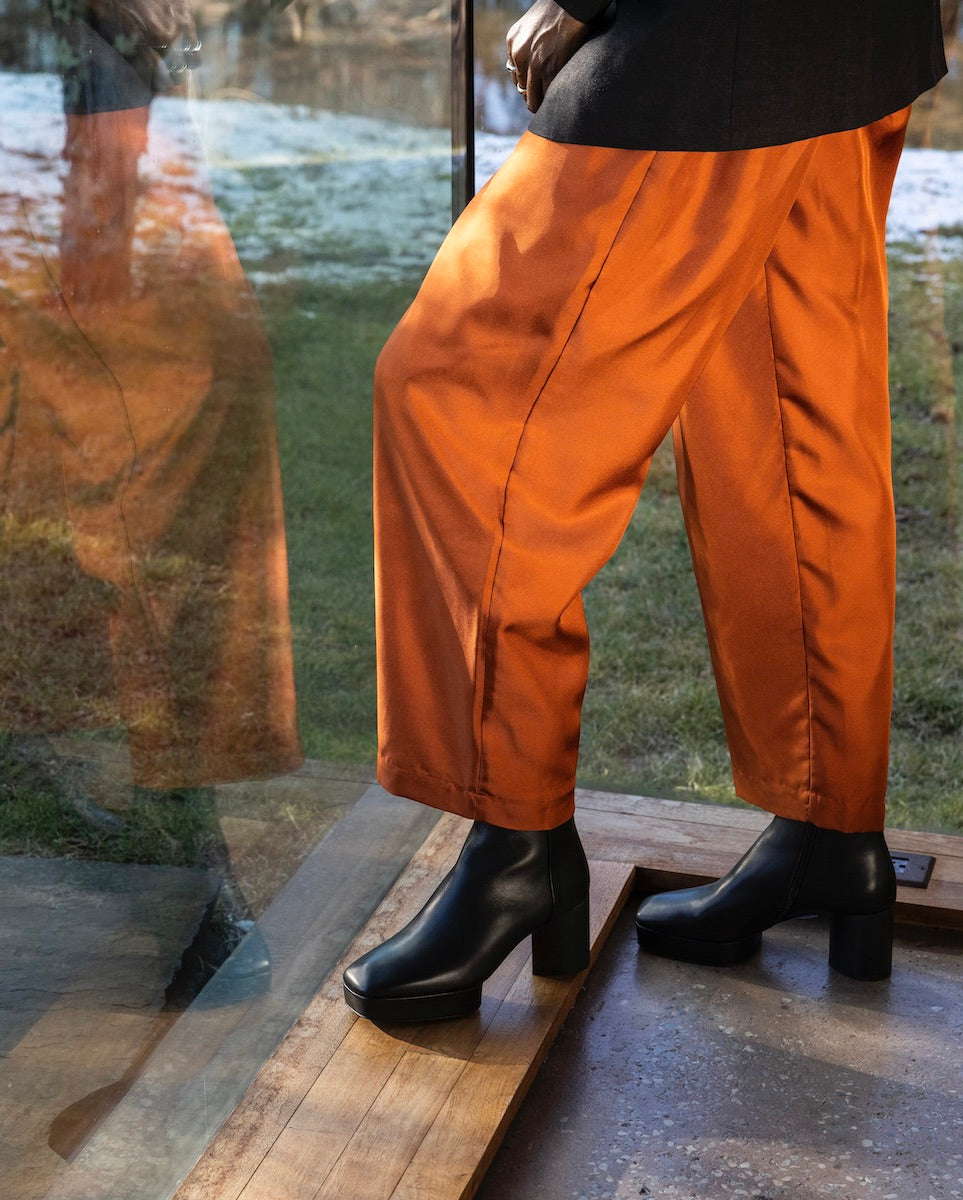 Women's legs wearing orange pants with the Travis Boot in Black while facing outside.