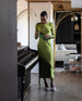 Woman wearing a green silk dress and the Trinity Pump in Milky Way while standing next to the piano.  5