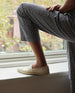 Woman modeling with leg up on window sill in the Coclico Udo Sneaker in Greige leather: cap-toe loafer style sneaker, low profile rubber sole, pointed toe.  4