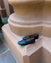 A slip-on, form-fitting flat in Italian certified sustainable leather with a squared-off toe and a 10mm solid wood heel, placed on a terracotta pillar - side view.  5