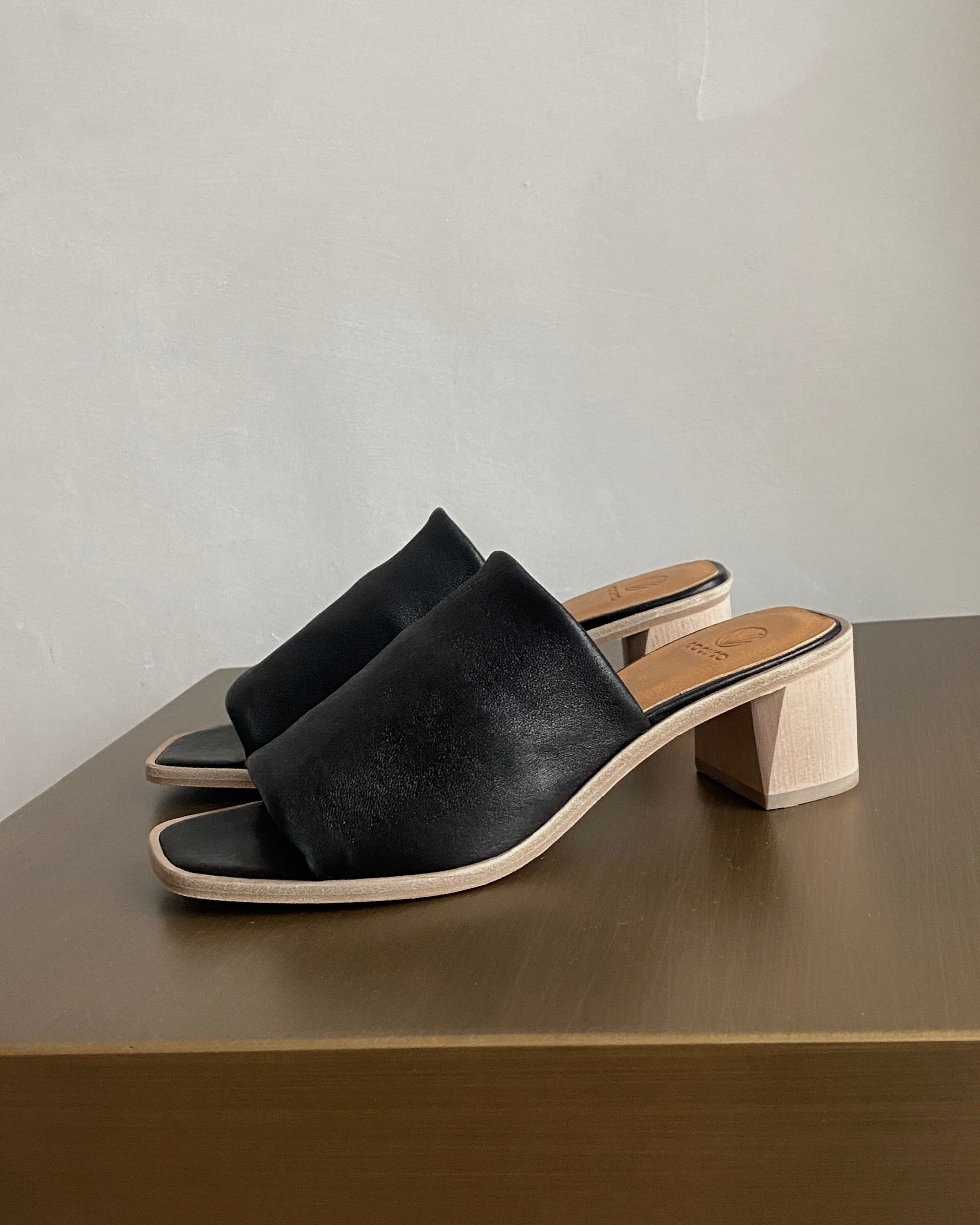 Close up angle view of the Coclico Jacque Heel in Black leather: slide-on style with a stretch leather band across foot and a wood block mid-height heel.