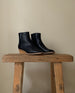 Angled view of the Java Boot in Black placed on a wooden stool.  10