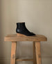 Side view of the Java Boot in black placed on a wooden stool.  9