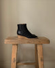 Side view of the Java Boot in black placed on a wooden stool. 9