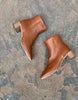 Top view, close up of the Coclico Juju Boot in Caramello leather, a minimalist boot featuring an inside zip closure, soft squared-off toe, mid-height solid wood block heel, mid-height shaft - on stone flooring. 6