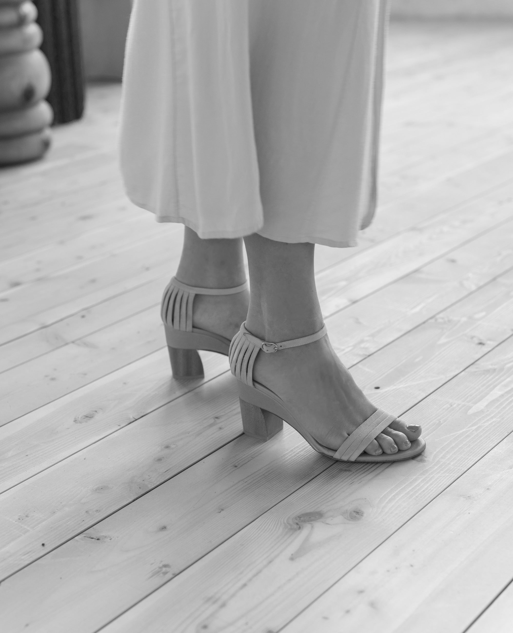 Black & white close up of Coclico Iris Heel in Greige leather: 3 thin straps across front of the foot, fan effect of straps cupping heel, leather-wrapped demi-wedge, mid-height walnut wood heel - side view.