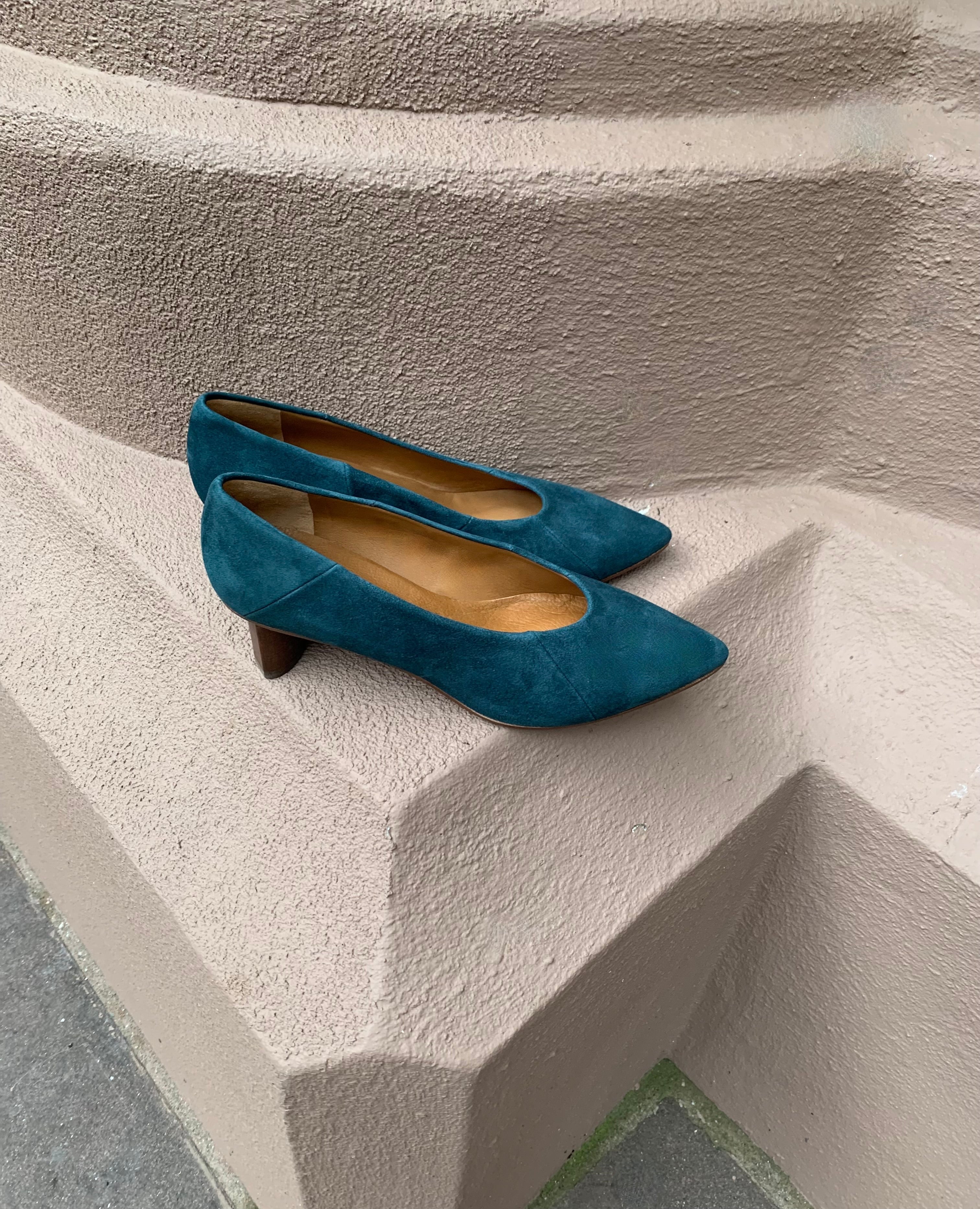 A seasonless slip-on heel with a choked throat line, subtle stichwork and a scultped, oval shaped solid wood heel with a hand-painted chestnut finish - Coclico Wumo Heel displayed on terracotta pillar.