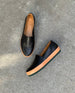 Close up of Coclico Gentian Flat in Black leather on cement floor: Slip-on flat with leather band and .5 inch rubber EVA sole. 5