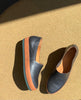 Top view close up of Coclico Gentian Flat in Black leather: a closed toe slip-on flat with leather band and .5 inch rubber EVA sole - in sunlight with cork flooring. 7