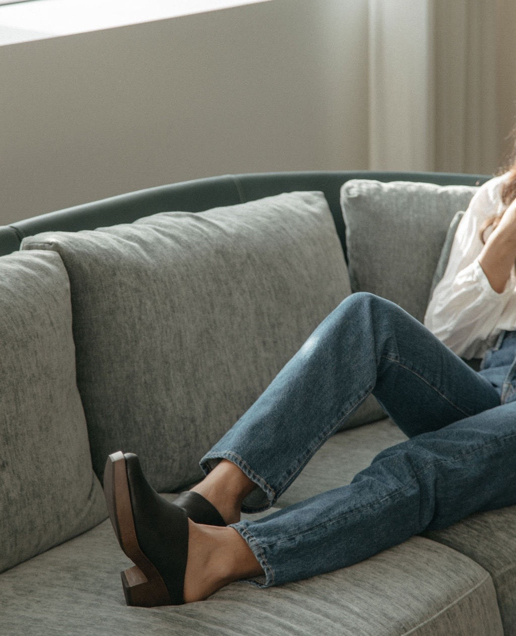 View of women's upper body and legs laying on a couch wearing jeans and a white shirt with the Kera Shearling Clog
