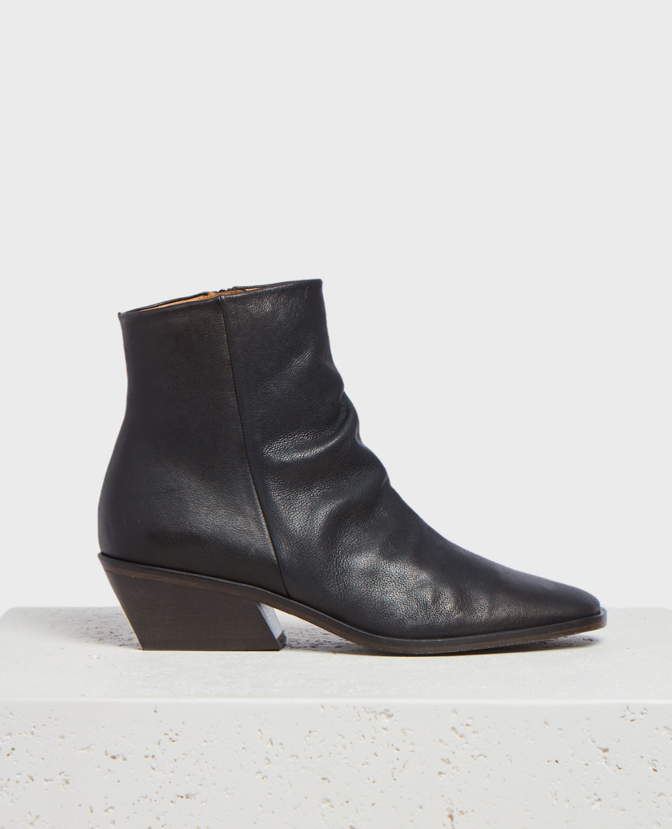 A sleek black leather ankle boot with a pointed toe, featuring a textured surface, a side zipper, and a distinctive angled wooden block heel.