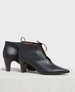 A pair of sleek, black leather ankle boots with a pointed toe, mid-height cone heel, and a front lace-up detail. 1