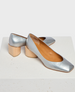 A pair of sleek, metallic silver leather shoes with a square toe design, featuring a low, chunky wooden heel and a smooth, tan interior lining. 1