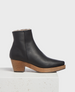 A sleek black leather ankle boot with a smooth texture, featuring a rounded toe, a wooden block heel, and a soft, fur-lined interior. 2