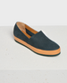 A dark blue suede slip-on shoe with a contrasting tan rubber sole, featuring a low heel and a smooth, minimalist design. 1