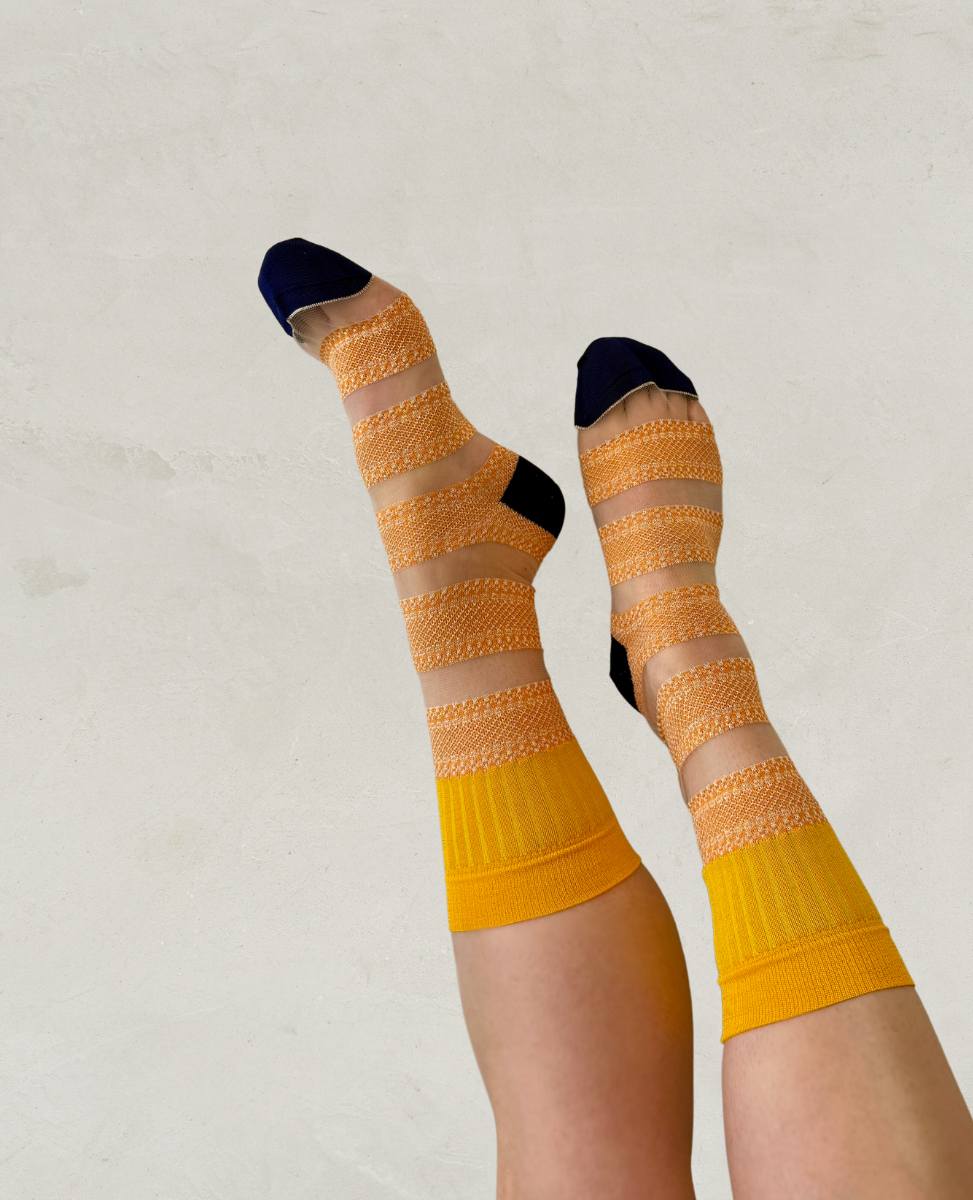 Knee-high socks featuring alternating bands of sheer beige mesh and textured orange knit, with solid yellow cuffs and dark blue toes and heels.