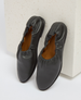 A pair of black leather slip-on shoes with a ruched elastic top, smooth texture, rounded toe, and a contrasting tan interior lining. 1