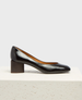 A sleek, black patent leather pump with a rounded toe, featuring a low, chunky block heel and a smooth, glossy finish. 3