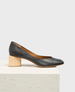 A sleek black leather pump with a rounded toe and a distinctive cylindrical wooden heel, featuring a smooth texture and a minimalist design. 1