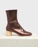 A metallic brown ankle boot with a smooth, shiny texture, featuring a rounded toe, a side zipper, and a distinctive light wooden block heel. 3