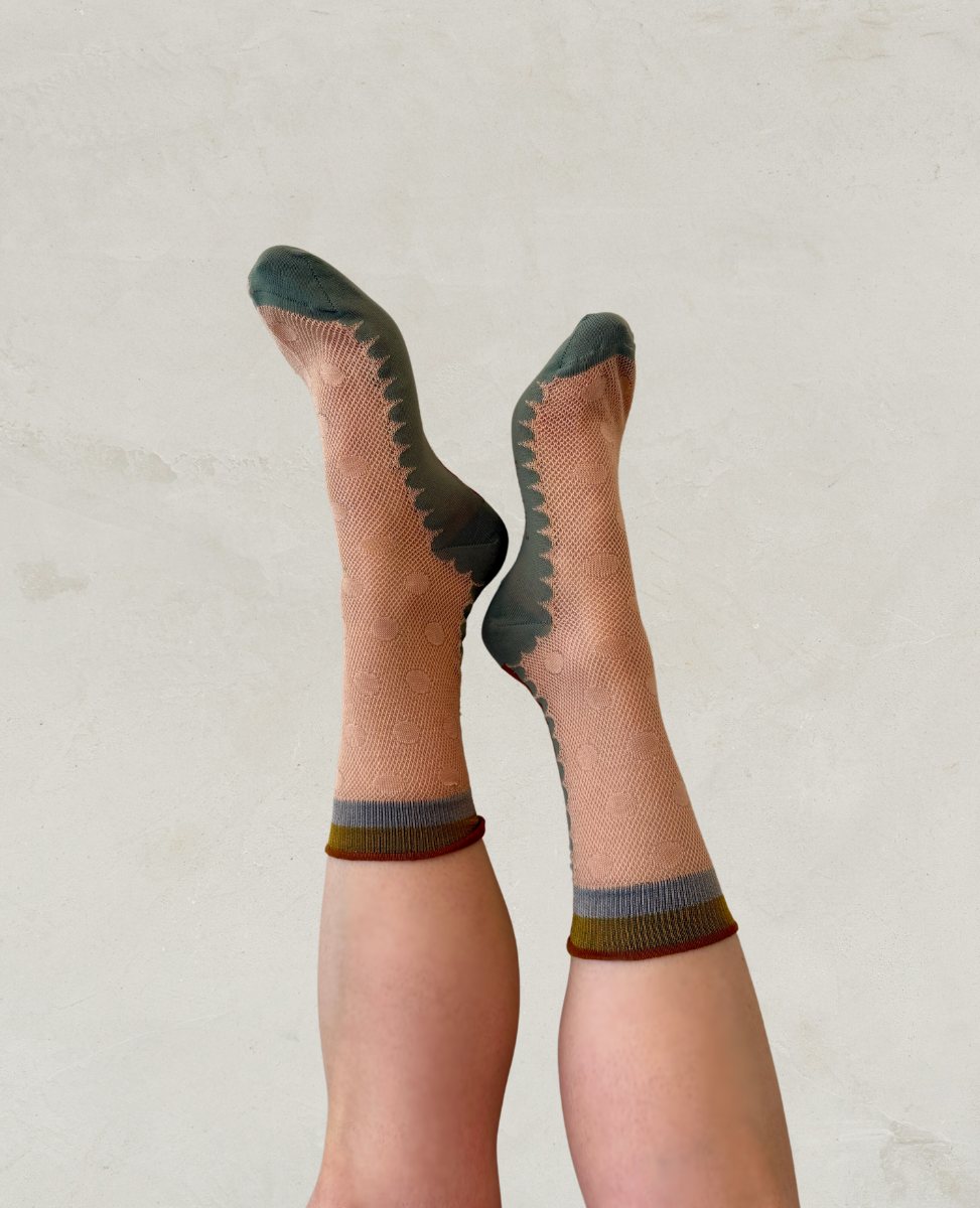 A pair of feet wearing light brown socks with dark green toes and heels, featuring a zigzag pattern along the sides and a mustard yellow band at the top.
