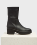 A sleek black leather boot with a mid-calf height, featuring a smooth, matte texture, a rounded toe, and a chunky block heel on a sturdy rubber sole. 1