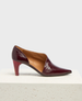 A sleek, burgundy patent leather shoe with a pointed toe, mid-height stiletto heel, and smooth, glossy texture, featuring a subtle seam detail along the side. 1