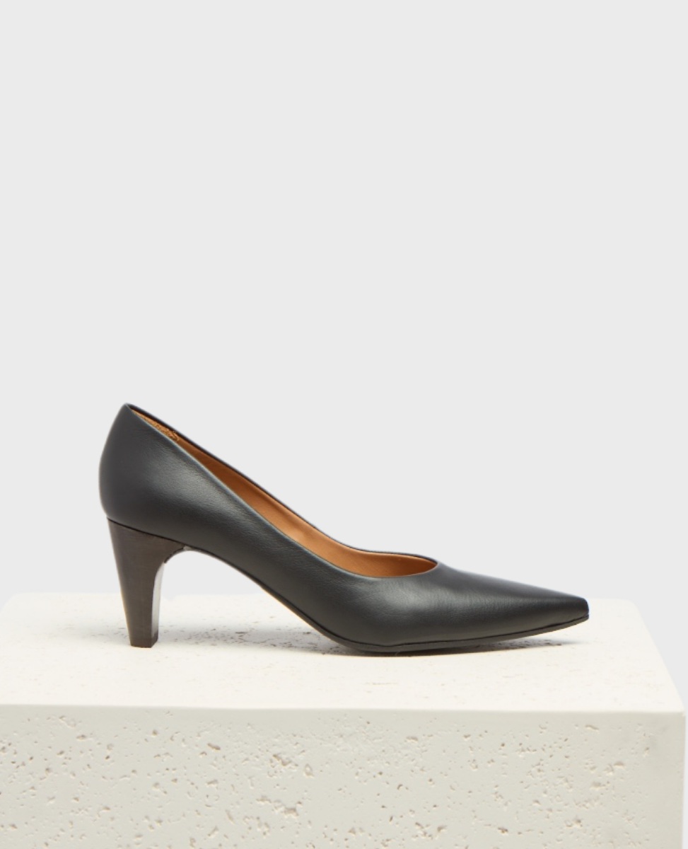 A sleek black leather high-heeled shoe with a pointed toe, smooth texture, and a medium-height stiletto heel, resting on a textured white surface.