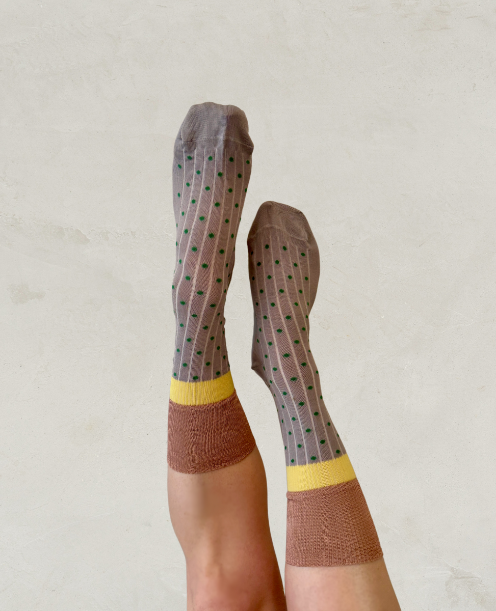 A pair of mid-calf socks with a brown base, featuring a pattern of small green dots, a yellow band near the top, and a solid brown section at the toes and heels.