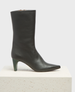 A sleek, black leather ankle boot with a pointed toe, mid-calf height, and a unique green tapered heel, featuring a smooth texture and a minimalist design. 1