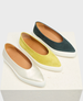 Three pairs of slip-on shoes with a sleek, pointed toe design feature a smooth, shiny silver pair, a soft, suede-like yellow pair, and a dark teal pair, all with contrasting white rubber soles and tan leather interiors. 5