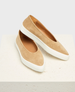 A pair of beige suede slip-on shoes with a smooth texture, featuring a sleek, rounded design and contrasting thick white rubber soles. 1