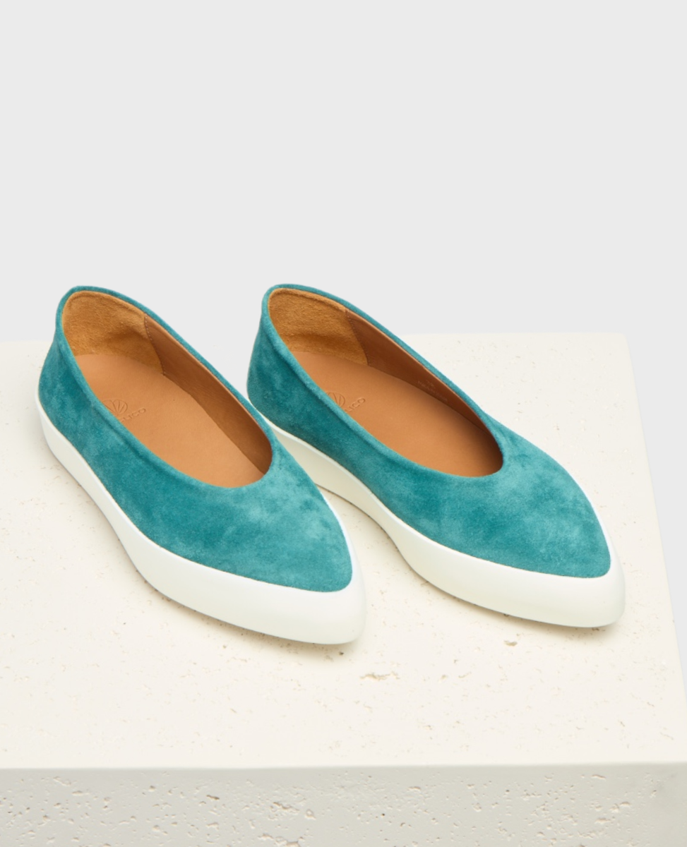 A pair of teal suede slip-on shoes with a smooth texture, featuring a pointed toe design and a contrasting white rubber sole.