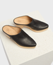 A pair of sleek, black leather mules with a pointed toe, featuring a smooth texture and a light wooden sole with a low heel. 6