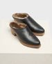 Black leather slip-on clogs with a wooden sole, featuring a plush brown fur lining and a slightly elevated heel. 3