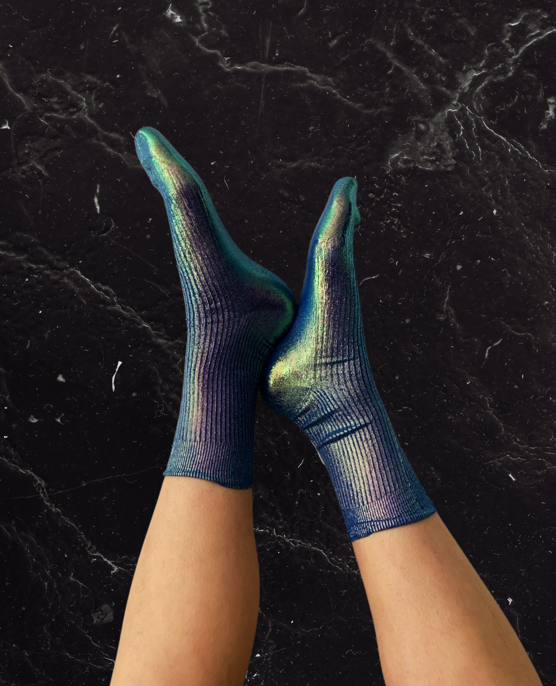 Feet wearing metallic foil silk socks against a black marble wall