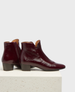 These ankle boots feature a glossy burgundy leather exterior with a sleek, rounded toe, a low block heel, and a side zipper for easy access. 1