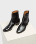 Sleek black ankle boots with a glossy finish, featuring a pointed toe, low block heel, and a subtle side zipper, crafted from smooth leather with a slightly textured surface. 2