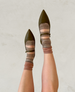 Pointed-toe olive green flats with a smooth leather finish feature a strap across the top, paired with patterned socks in shades of brown and beige. 1