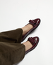 Shiny burgundy loafers with a sleek, rounded toe and a decorative strap across the top, featuring a low black sole and a smooth, polished leather finish. 2