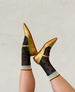 Gold pointed-toe flats with a glossy finish, paired with black mesh socks featuring large polka dots and green accents, worn on feet raised against a neutral background. 3