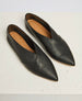 A pair of sleek, black leather flats with a pointed toe, smooth texture, and a unique overlapping design on the upper, featuring a tan insole with a subtle logo imprint. 1