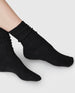 Another side angle of the Swedish Stockings Bodil wool socks in black shown on a model with her ankles crossed. 4