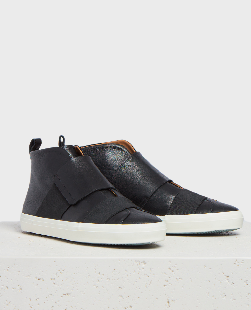 A pair of sleek, black leather high-top sneakers with a smooth texture, featuring wide overlapping straps across the front, a pull tab at the heel, and a contrasting white rubber sole.
