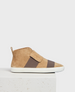 A tan suede high-top sneaker with a white rubber sole, featuring a wide brown elastic band across the midfoot and a pull tab at the heel. 1