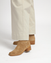 Tan suede boots with a block heel and squared toe, featuring a smooth texture and a wooden sole, paired with cream-colored wide-leg pants. 2