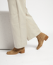 A pair of tan suede boots with a low wooden block heel, featuring a smooth texture and a sleek, minimalist design, worn with light beige wide-leg pants. 4