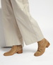 Tan suede boots with a squared toe, wooden block heel, and subtle stitching details, paired with wide-leg cream pants. 3