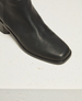 A sleek, black leather boot with a square toe, smooth texture, and a sturdy, low block heel. 5